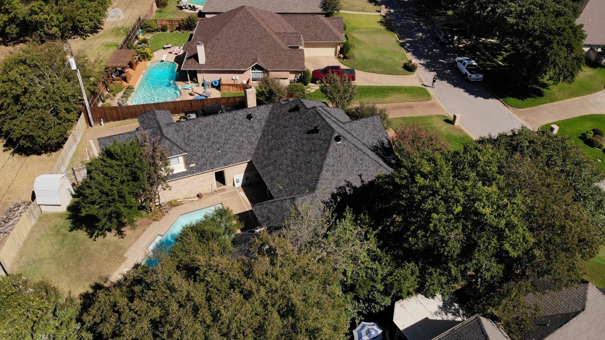 Drone view of a completed residential roof above a backyard pool and patio