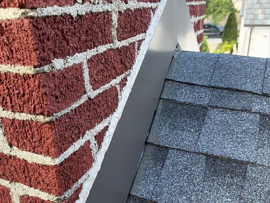 New metal step and counter flashing sealed against a brick chimney on a shingle roof
